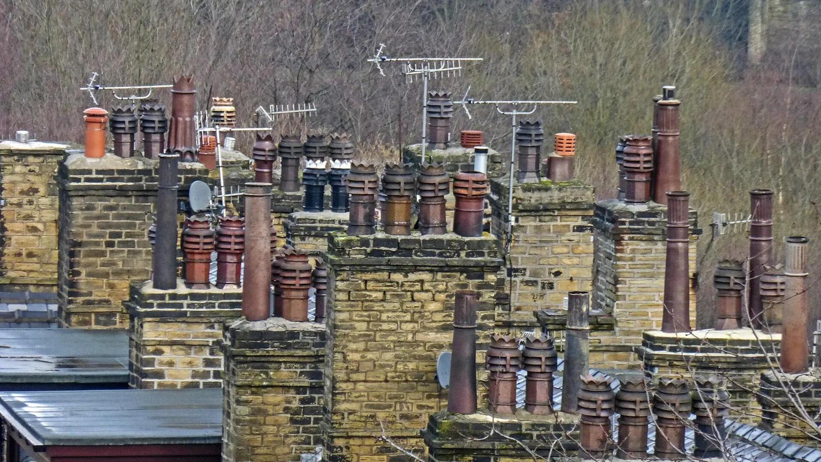 Clusters of stone and brick chimney stacks with terracotta chimney pots across terraced rooftops in a British town