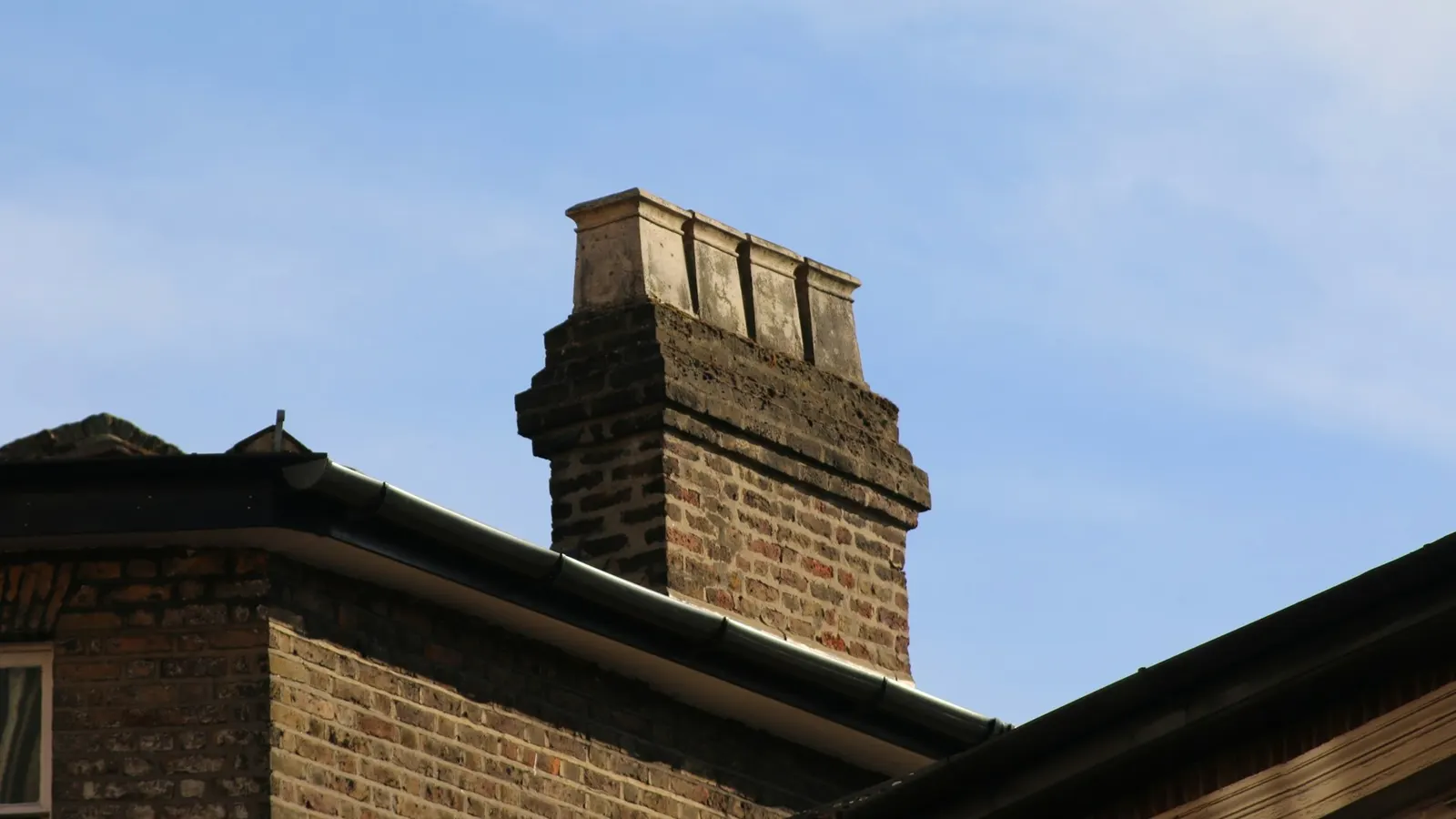 Brick chimney stack with corbelled courses and chimney pots on a London house in Ealing under blue sky