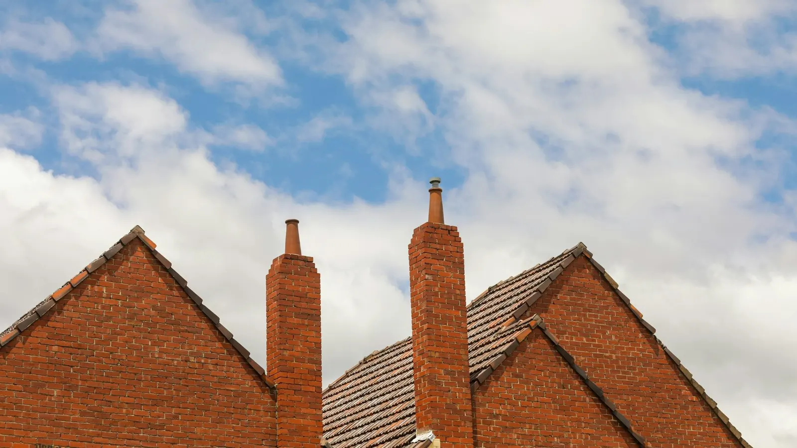 Red brick gable ends with tall brick chimney stacks on traditional British houses against a cloudy blue sky