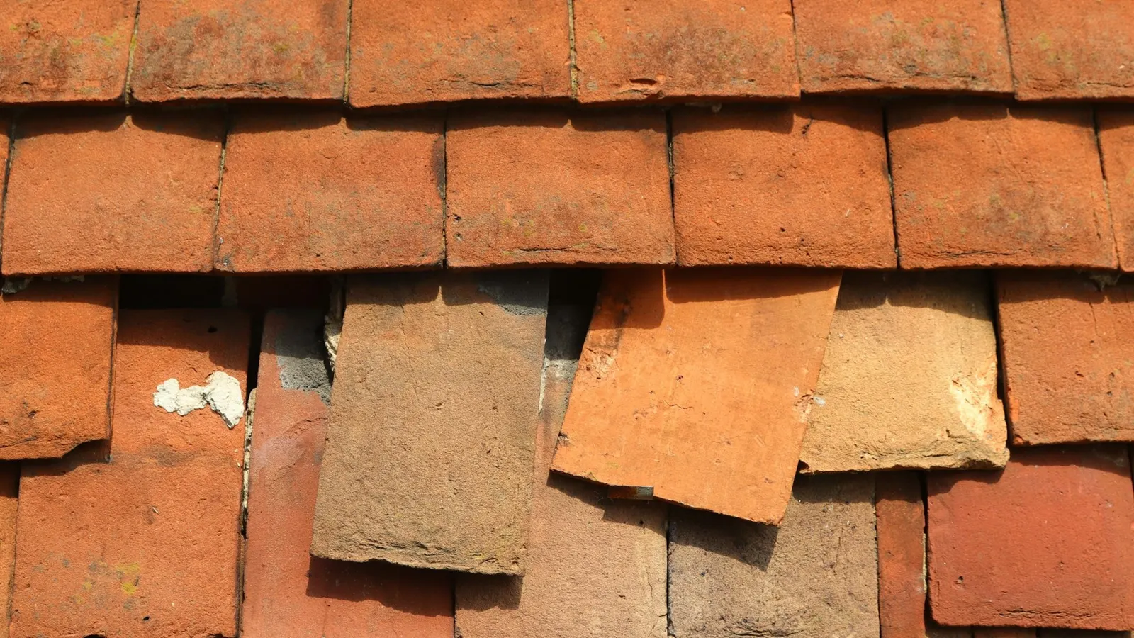 Slipped and broken plain clay roof tiles leaving gaps in a pitched roof