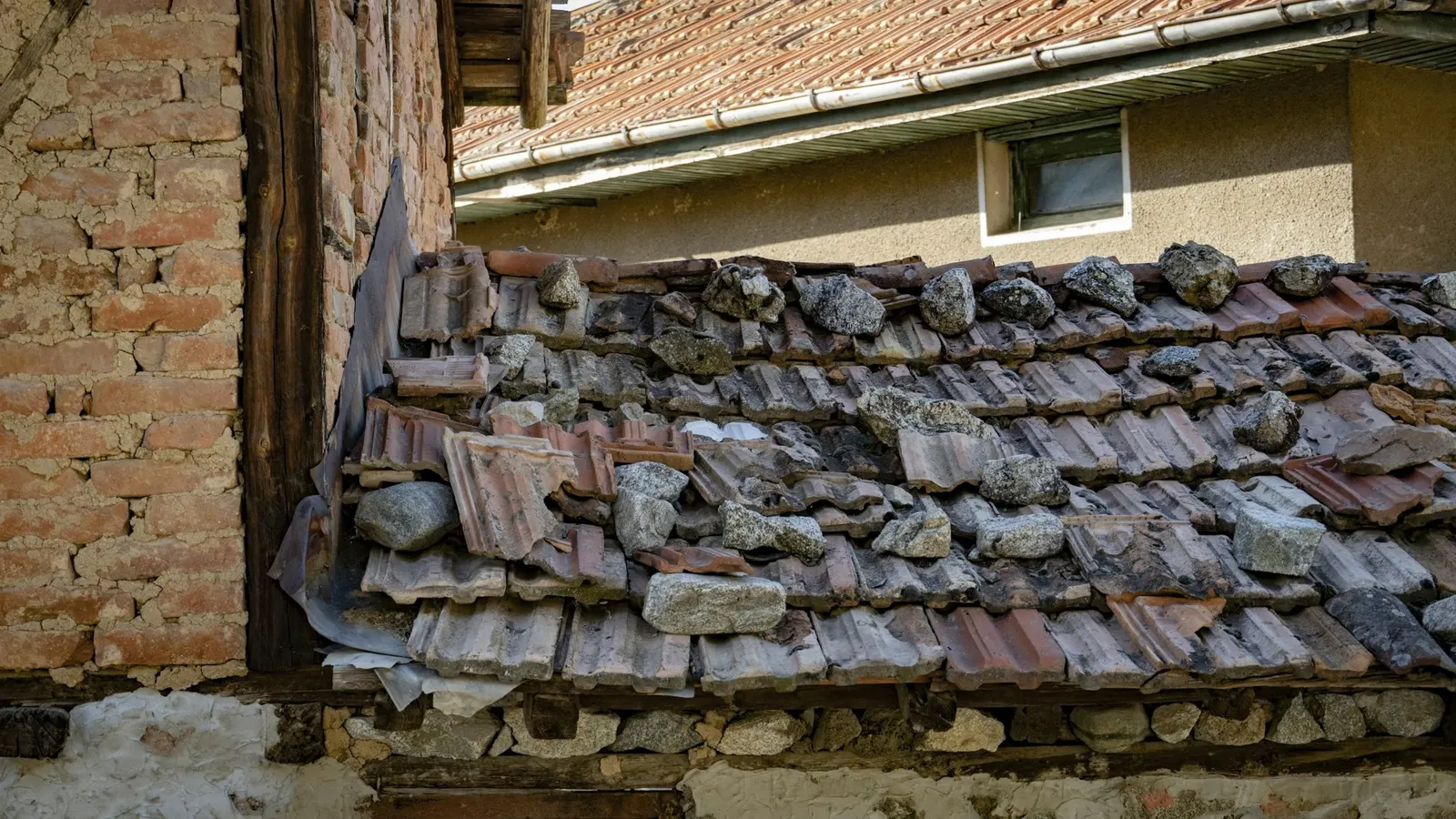 Storm-damaged tiled roof with displaced and broken tiles above a brick wall