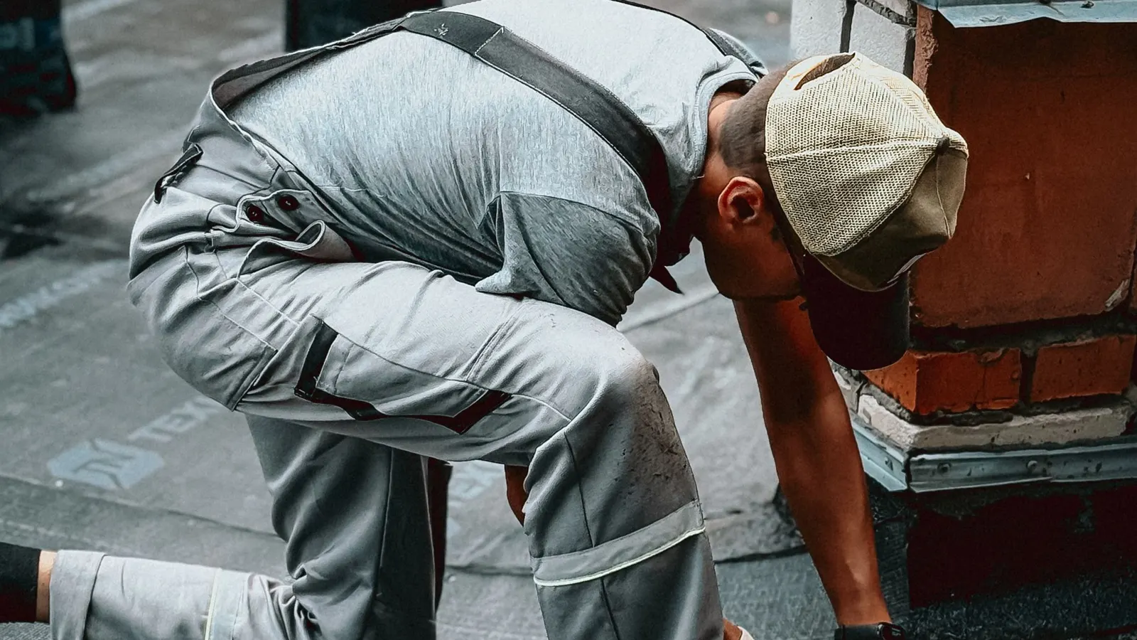 Roofer kneeling to work on a rubber membrane flat roof beside a brick chimney