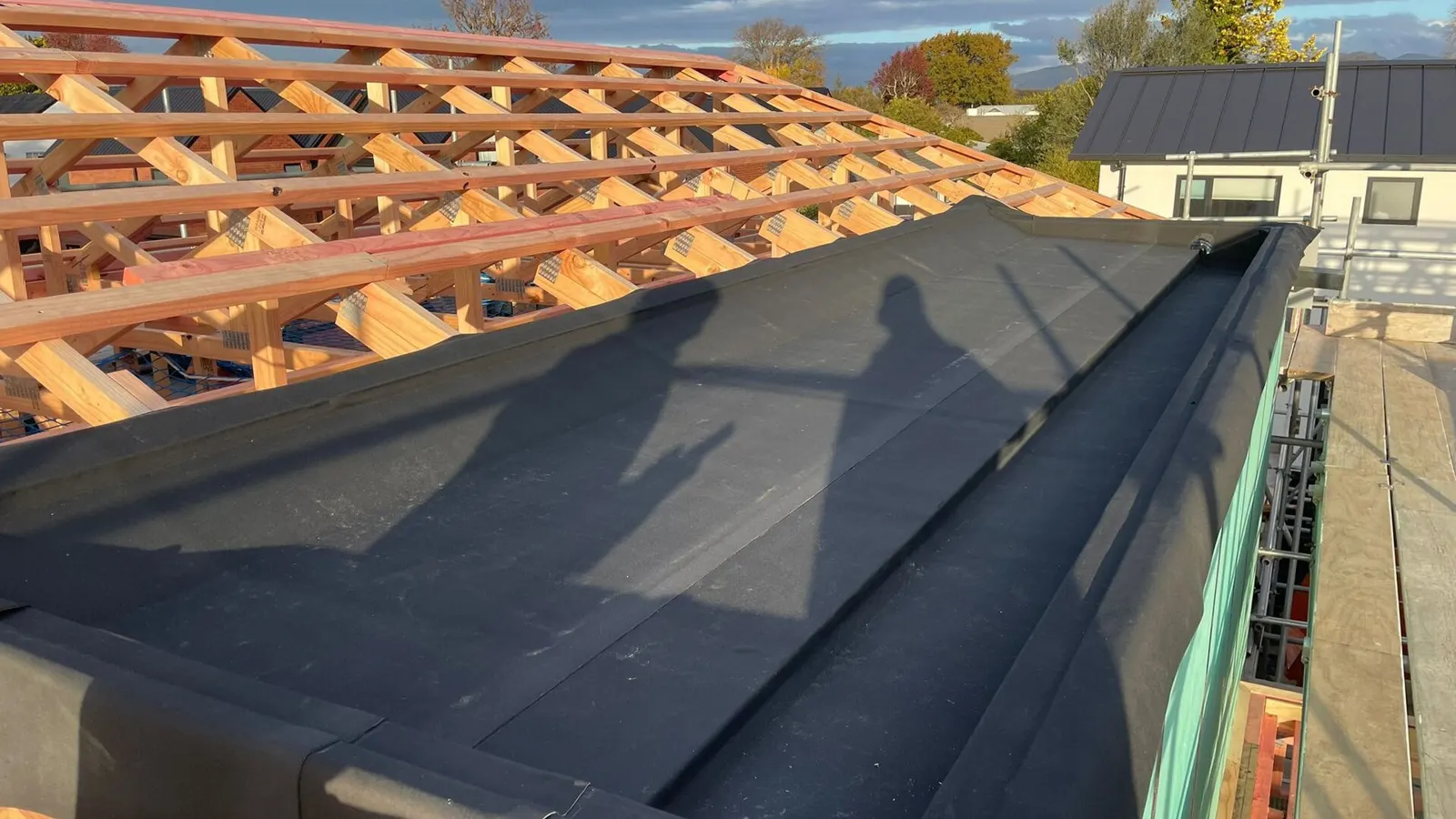 Black rubber roofing membrane being installed along a flat roof section during construction