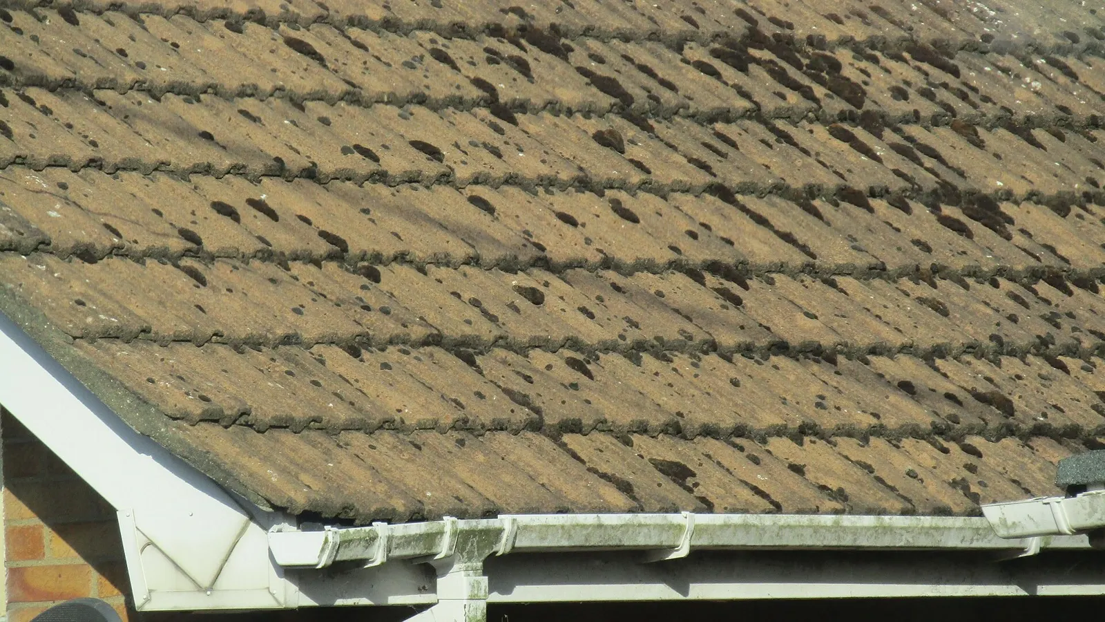 Close-up of plastic guttering running along the eaves beneath weathered clay roof tiles