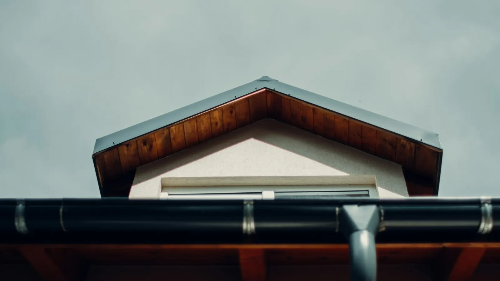 Black gutter with downpipe outlet running beneath a timber-clad gable roof