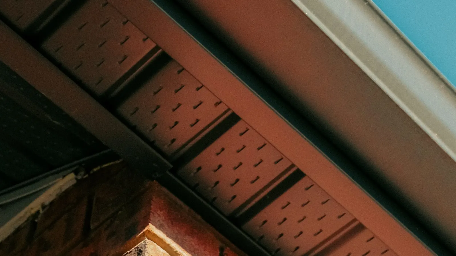 Underside view of vented soffit boards and fascia at the roof edge above a brick wall