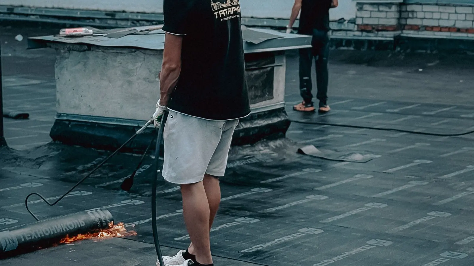 Roofers torching on bitumen felt to waterproof a flat roof