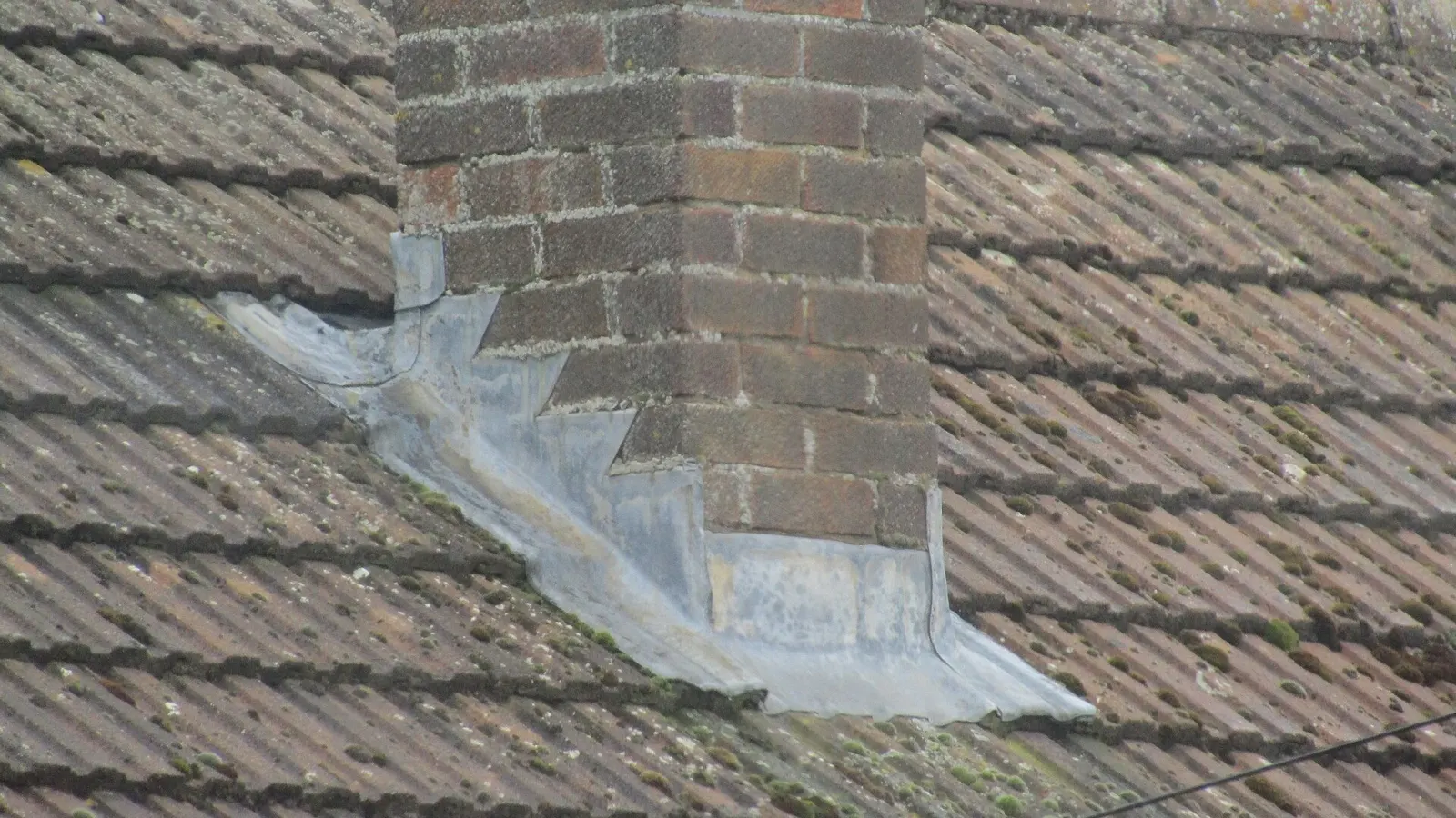 Lead flashing dressed around the base of a brick chimney stack on a pantile roof
