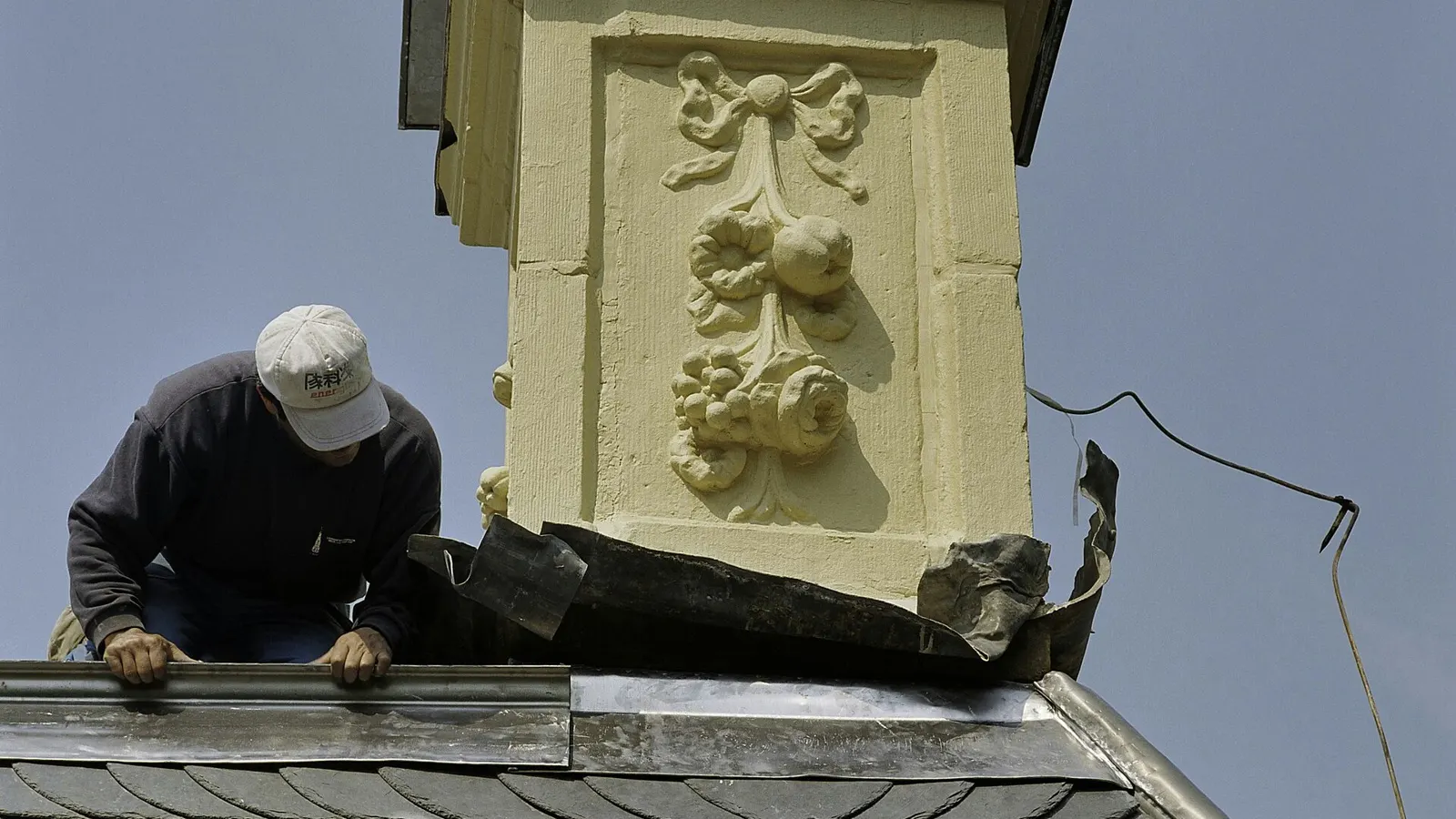 Roofer fitting new lead flashing around a chimney stack on a slate roof