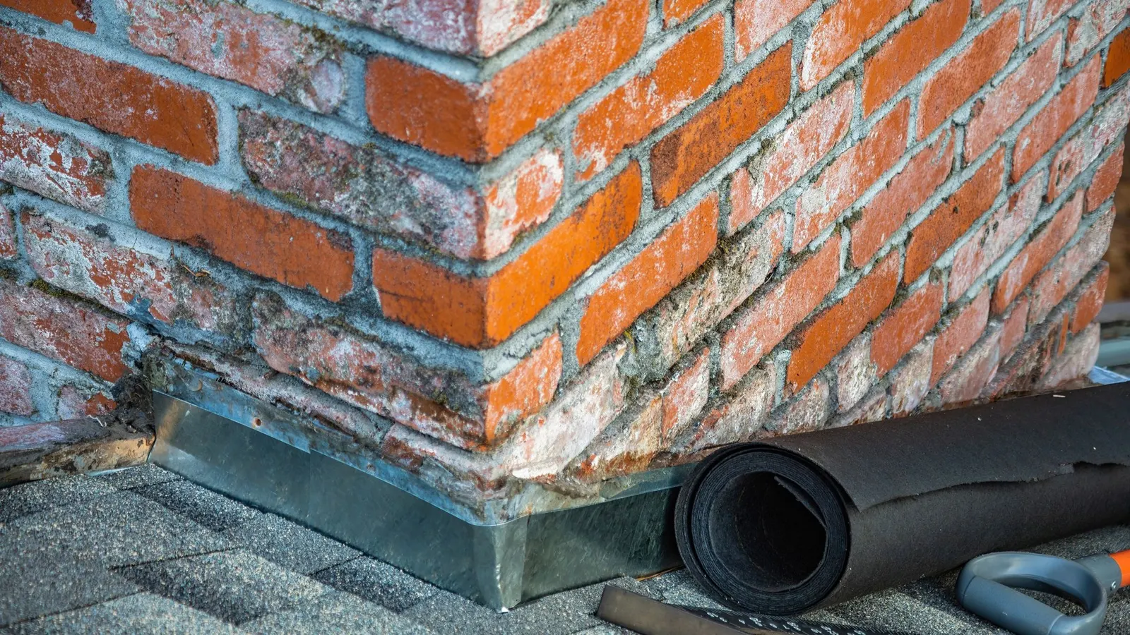 Close-up of lead flashing at the junction of a red brick chimney and roof with a roll of lead sheet