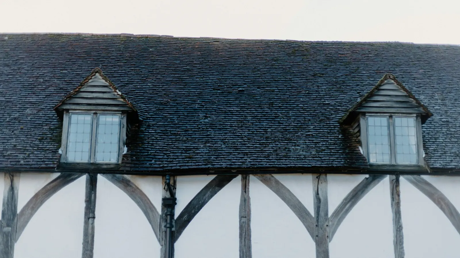 Slate roof with two pitched dormer windows and lead flashing details above a Tudor-style facade
