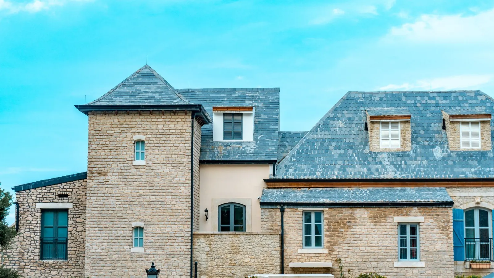 Stone house with blue slate roof and multiple dormers with lead-flashed junctions under clear sky