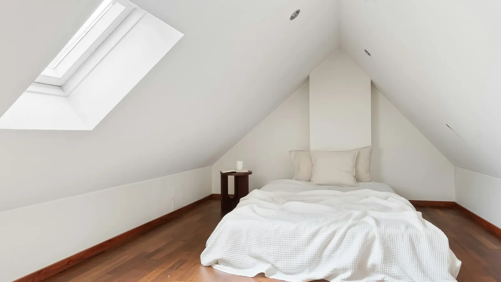 Bright converted loft bedroom with sloping ceiling and Velux roof window