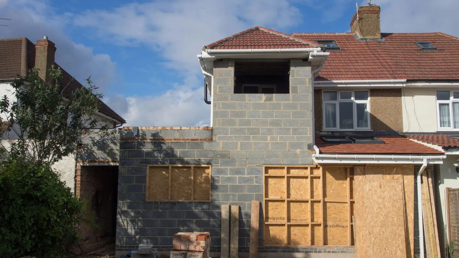 Semi-detached UK house mid-conversion, with new blockwork raising the roof and gable for a loft extension