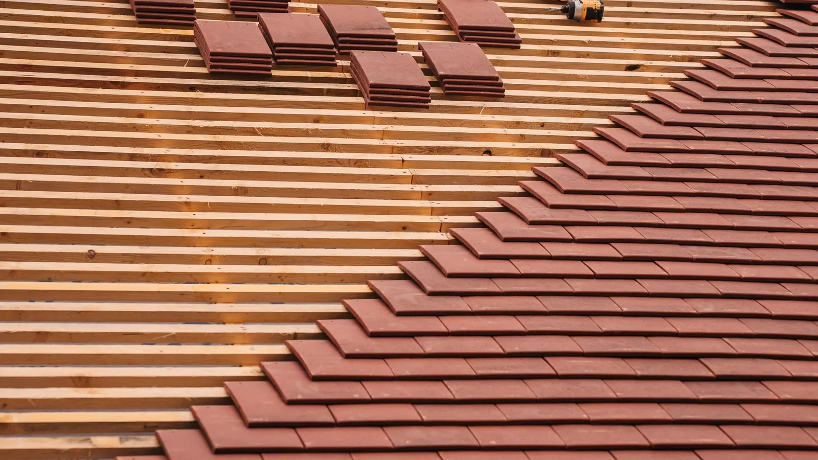 New terracotta plain tiles being fitted on a pitched roof, with spare tiles stacked on the slope