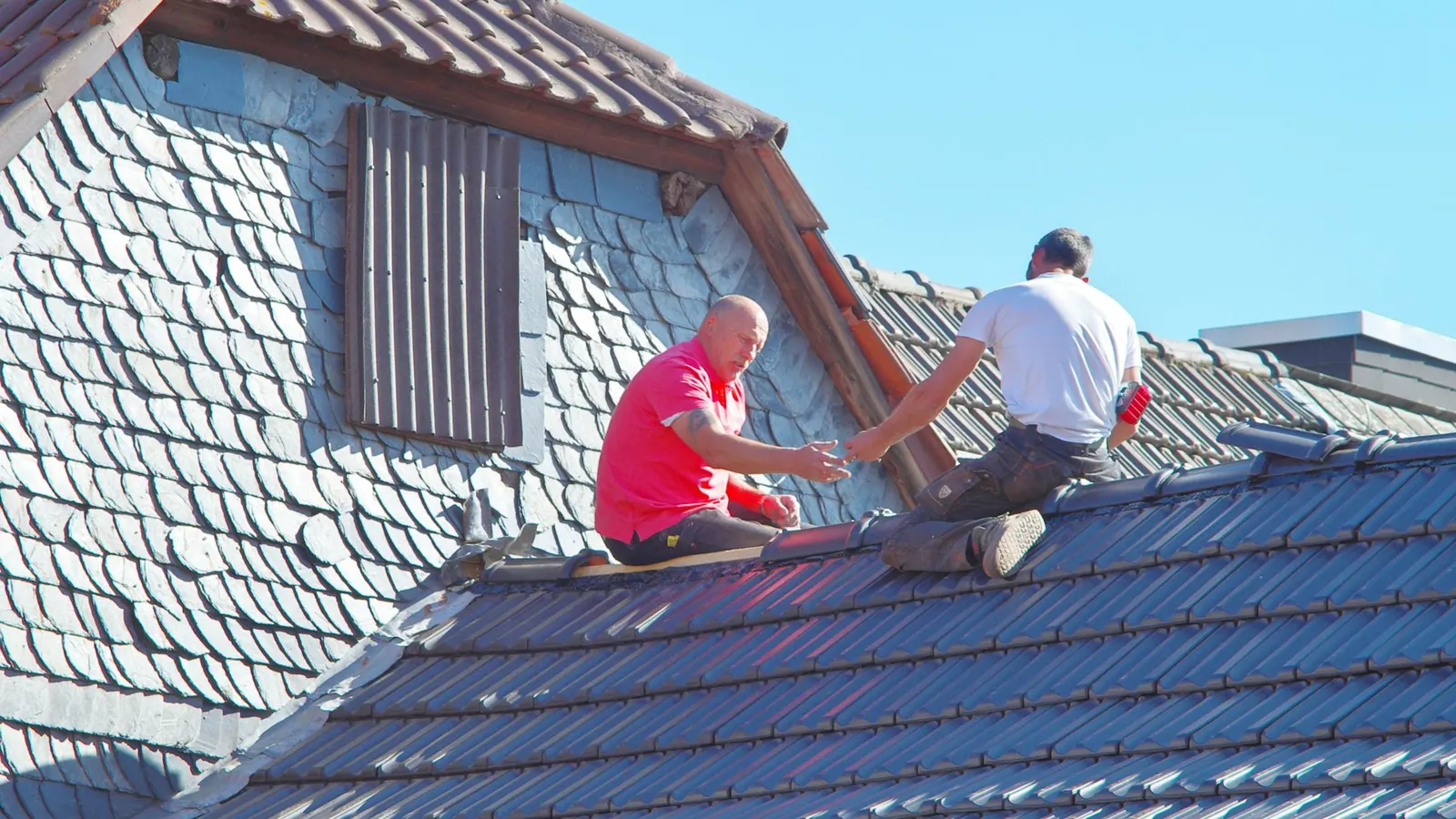 Roofers repairing a natural slate pitched roof beside a slate-hung dormer