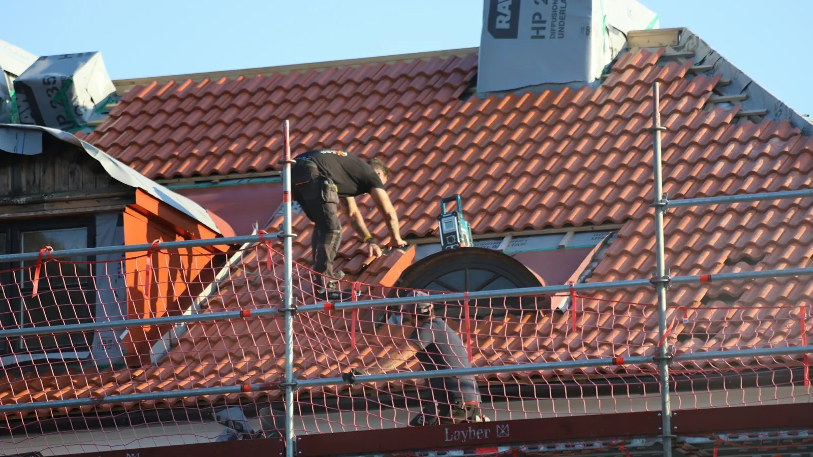 Roofer repairing a red clay tile roof from scaffolding on a house