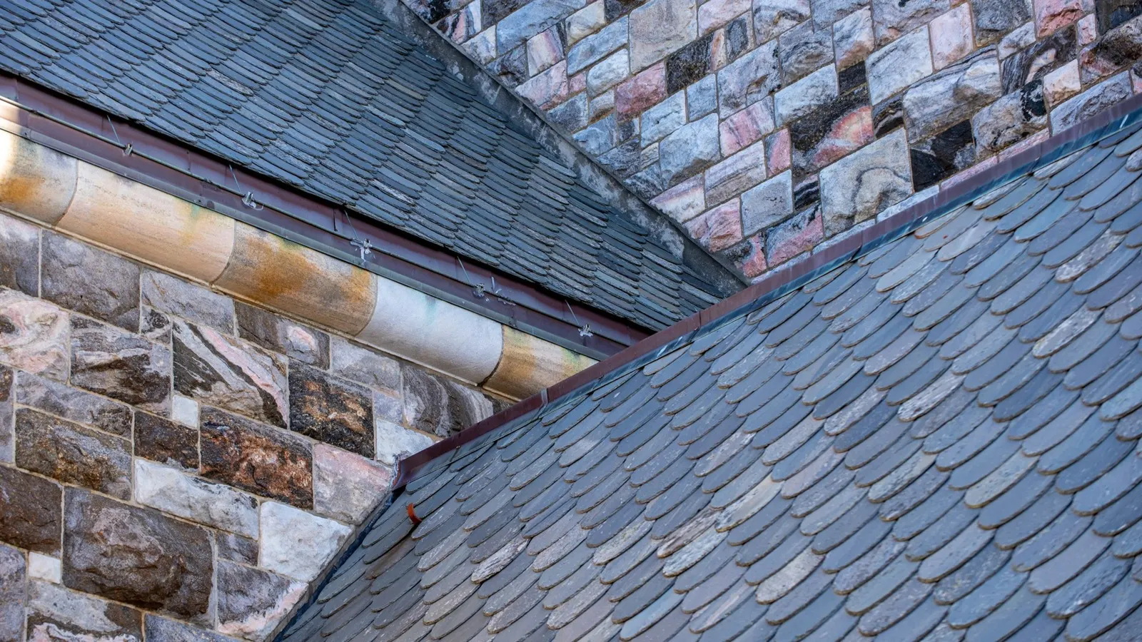 Slate roof valley meeting a stone wall, showing the slate and flashing detail