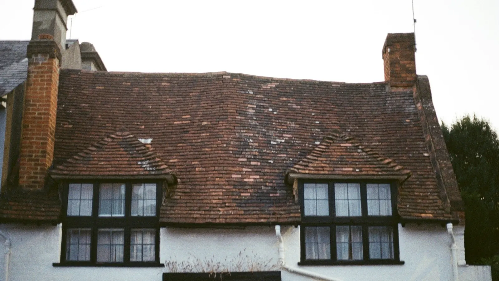Traditional English cottage with a weathered clay tile roof, twin dormers and brick chimneys